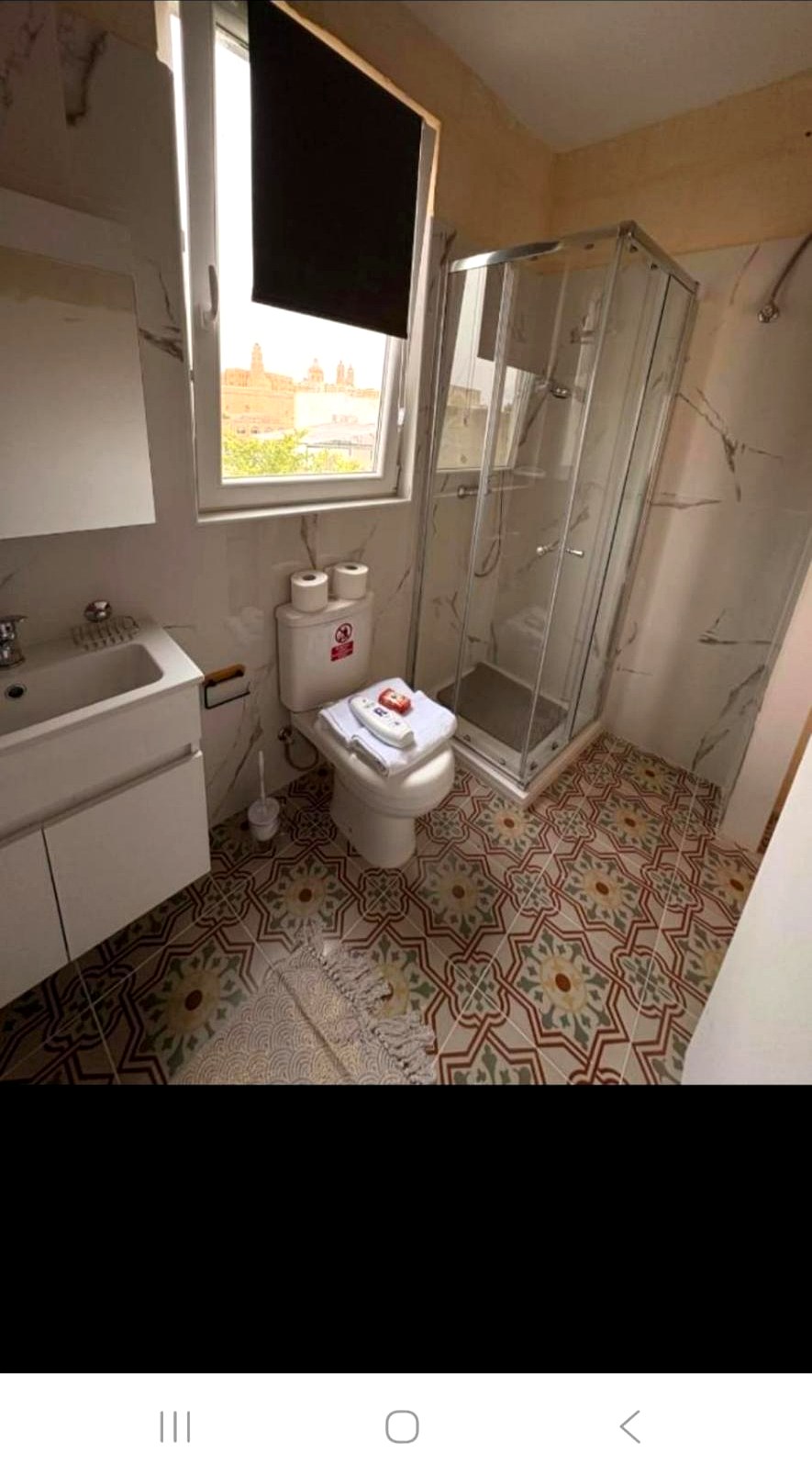 Marble bathroom with Maltese patterned tiles and a window framing the harbour view