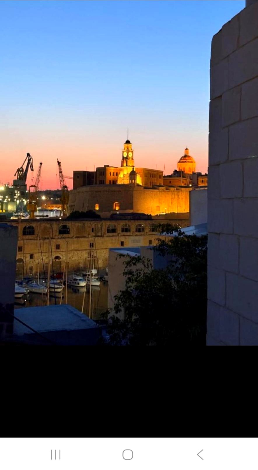 Sunset view over Cospicua harbour with illuminated clock tower and dome from the townhouse