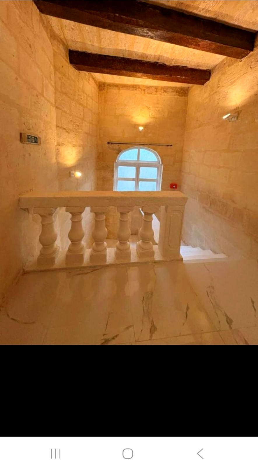 Limestone balustrade landing with exposed wooden beams and arched window