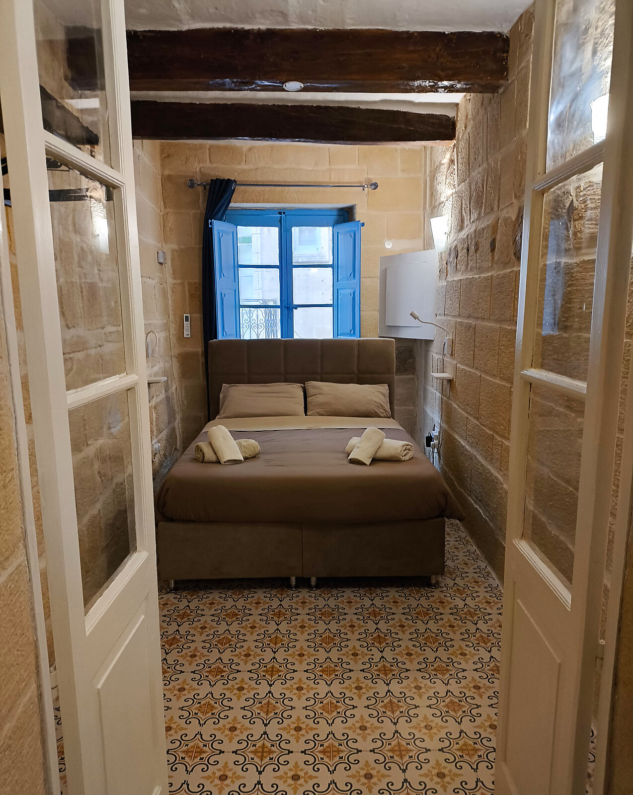 Bedroom seen through traditional French doors with stone walls and wooden beams