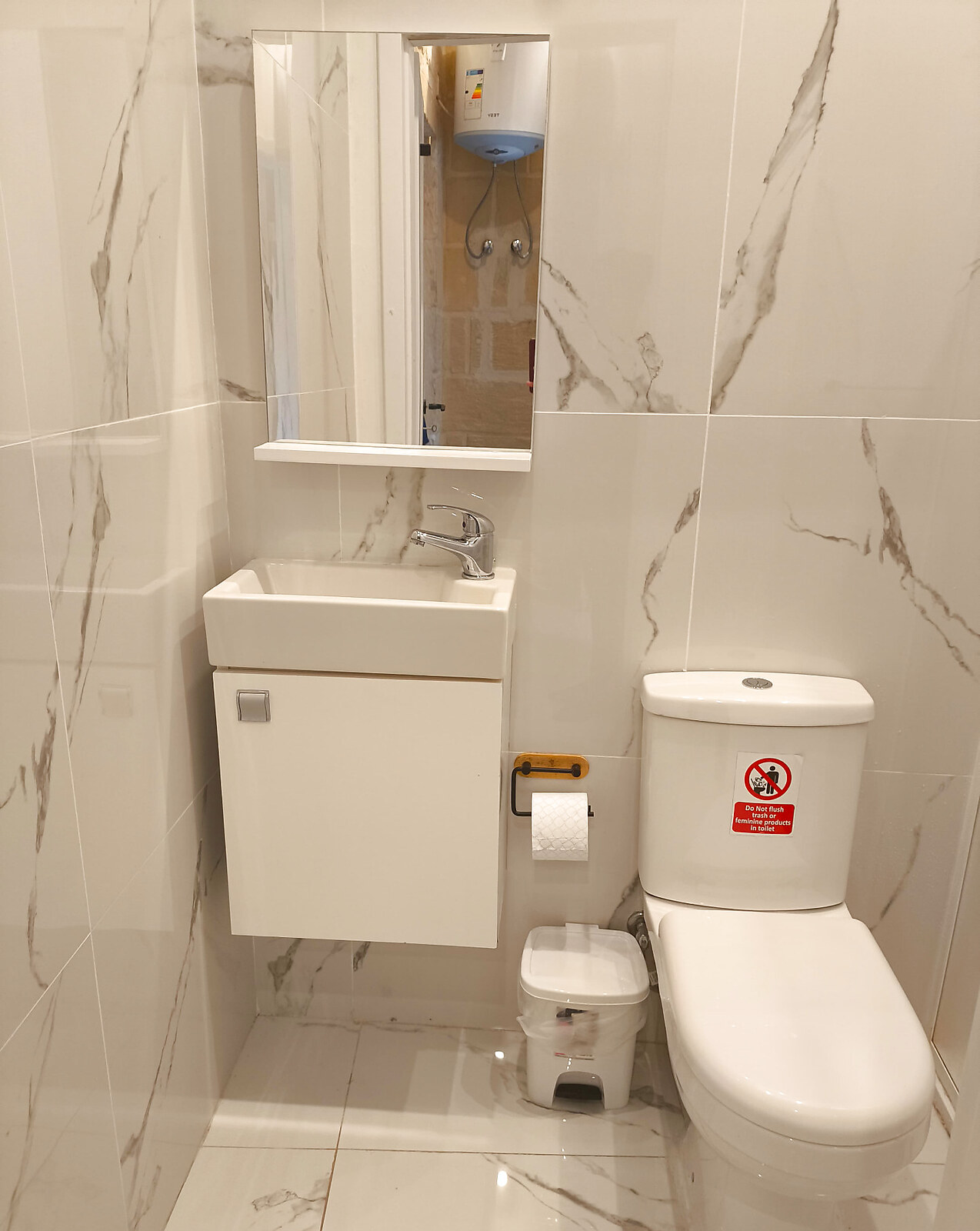Bright marble-tiled bathroom with white sink, mirror and toilet