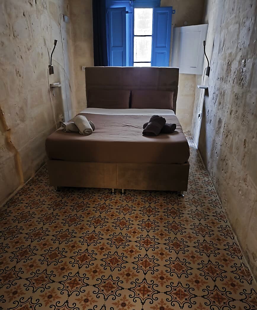 Cozy double bedroom with blue Maltese shutters and patterned tile floor